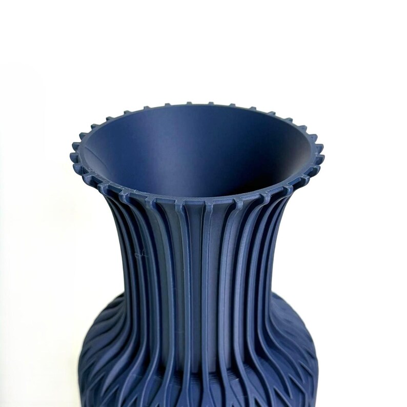 May include: A dark blue vase with a wide, flared rim featuring a series of small, evenly spaced vertical notches along the edge. The body of the vase is characterised by a repeating pattern of deep, vertical fluted ridges that extend downwards.