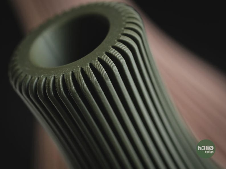 May include: An olive green cylindrical object with a hollow centre and a series of vertical, parallel ridges running along its exterior. The surface features a fine, textured finish. A small circular logo with the text h3li&oslash; design is visible.