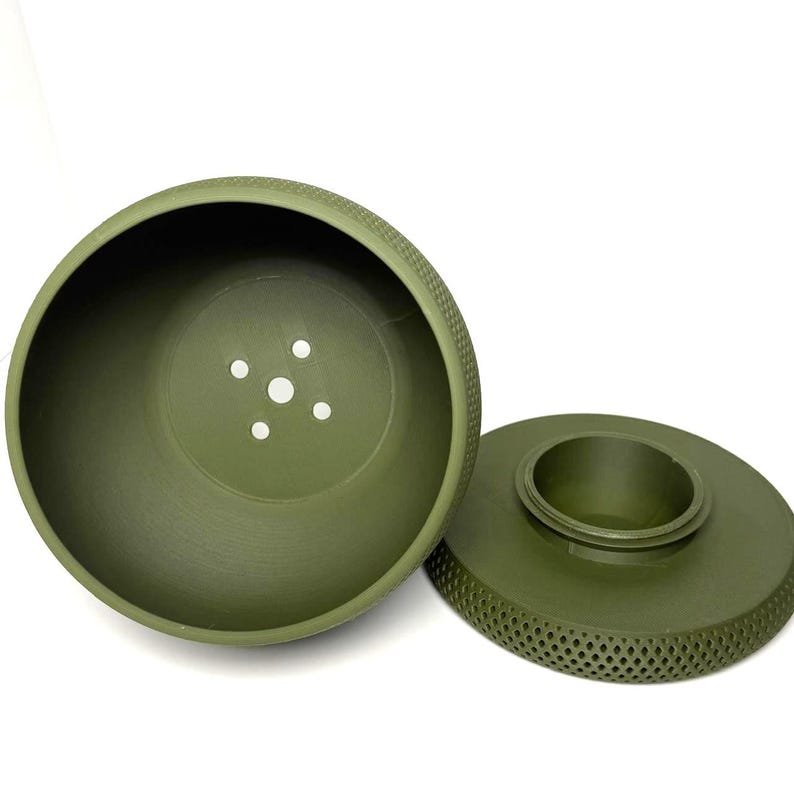 Puede incluir: Una maceta redonda de pl&aacute;stico de color verde oliva, compuesta por dos piezas con un exterior texturizado de patr&oacute;n de diamantes. El cuenco principal tiene cinco orificios de drenaje en la base y la base circular separada tiene un anillo central.