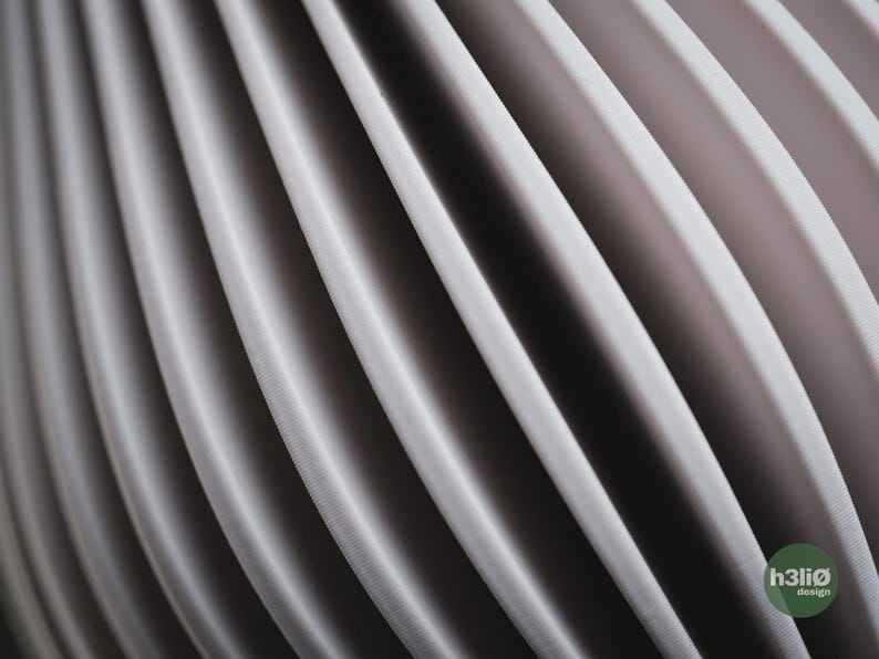 May include: A series of repeating, curved, light grey vertical panels creating a rhythmic, wave-like pattern. The surface of each panel has a fine, textured finish. A small circular green logo in the bottom right corner displays the text h3li&oslash; design.