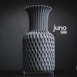 May include: A matte grey vase with a vertical ribbed neck and a diamond-patterned lattice texture on the body. The text "juno vase" is printed in white near the top, and a circular green logo with "h3li&oslash; design" is visible in the bottom corner.
