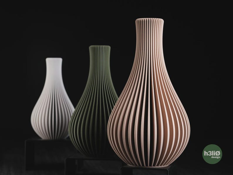 May include: Three vases with a vertical ribbed texture and a tapered neck. The vases are white, olive green, and light peach in colour. Each vase stands on a small black rectangular base. The text h3li&oslash; design is visible in the bottom right corner.