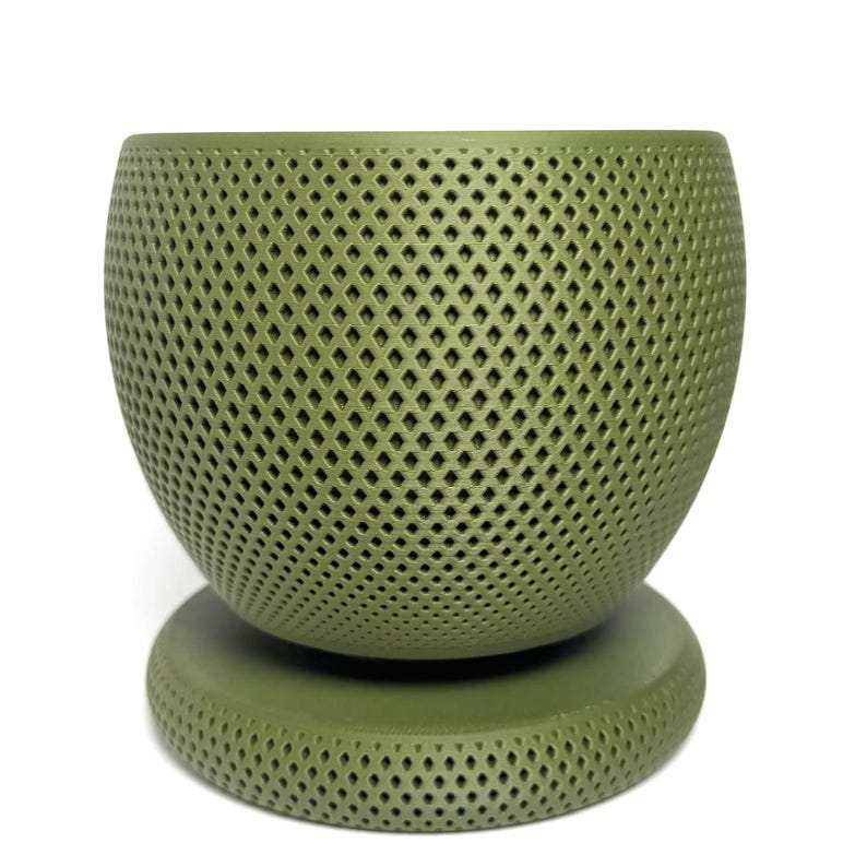 Puede incluir: Una maceta esf&eacute;rica de color verde salvia con un patr&oacute;n de celos&iacute;a en forma de diamante texturizado en toda su superficie. La maceta se asienta sobre una base circular a juego que presenta el mismo dise&ntilde;o geom&eacute;trico recortado y uniforme.