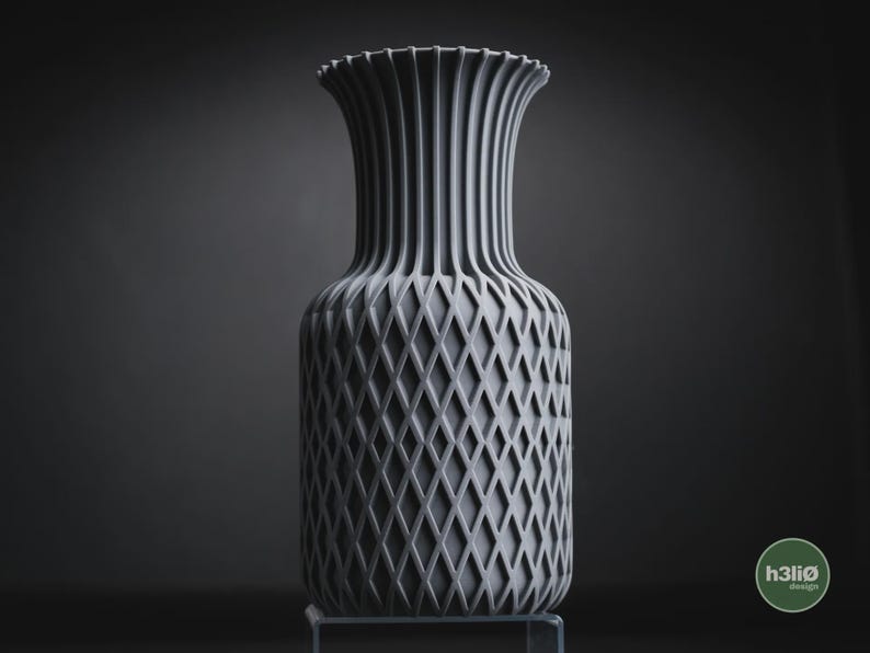 May include: A matte grey vase featuring a vertical ribbed neck and a textured diamond lattice pattern on the body. The base of the vase is cylindrical, and a small circular logo with the text h3li&oslash; design is visible in the bottom right corner.