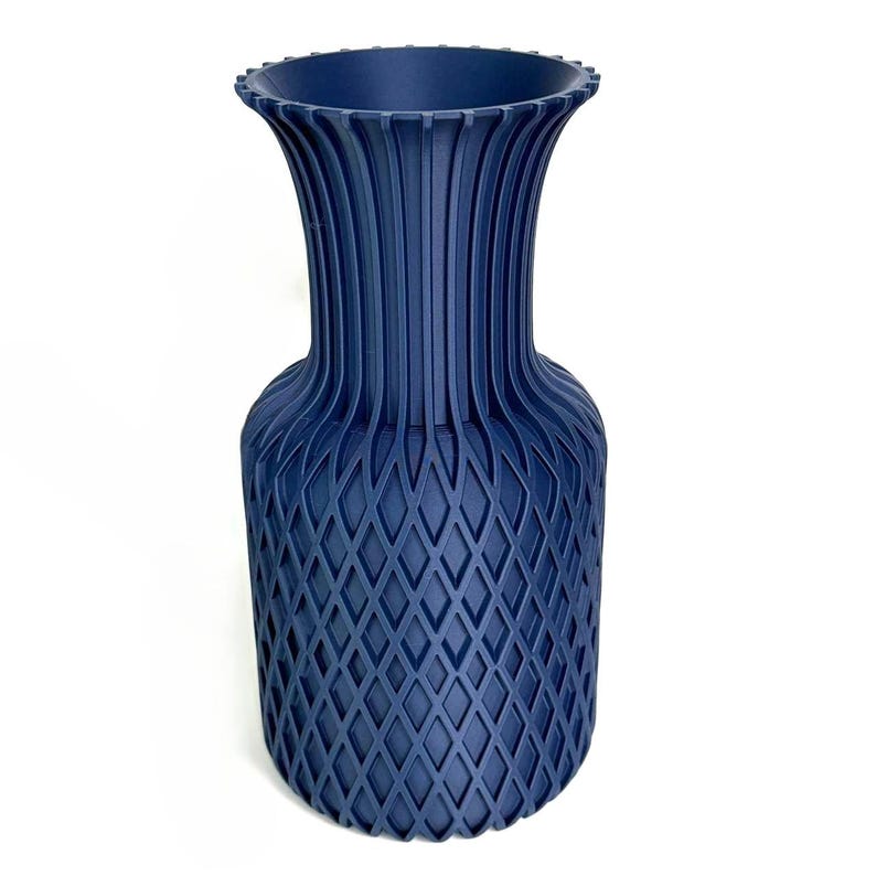 May include: A dark blue vase featuring a textured diamond lattice pattern on the lower body and vertical fluted ridges extending up to a flared, notched rim. The object has a matte finish and a consistent deep navy colour throughout its structure.