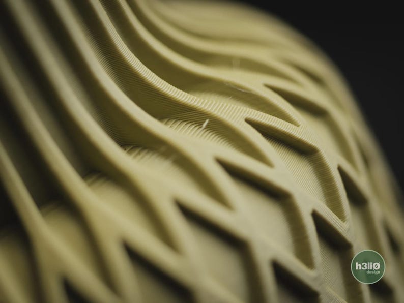 May include: A light olive green object featuring a repeating geometric pattern of raised, wavy ridges and interconnected diamond shapes. The surface texture shows fine, parallel lines from a 3D printing process. A small circular logo reads h3li&oslash; design.