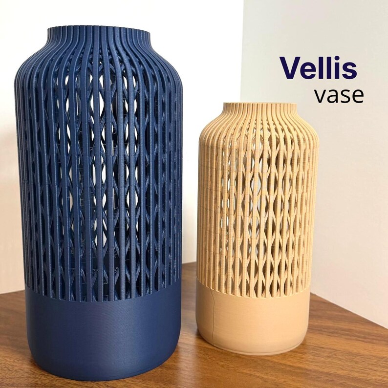 K&ouml;nnte beinhalten: Zwei Vellis-Vasen, eine dunkelblau und eine beige, mit einem massiven zylindrischen Boden und einem oberen Teil mit vertikaler Gitterstruktur. Der Text 'Vellis vase' ist in der oberen rechten Ecke des Bildes aufgedruckt.