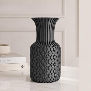 May include: A matte charcoal grey vase featuring a wide, flared rim and a textured, lattice-patterned body. The upper section of the vase displays vertical ridges that transition into a diamond-shaped grid pattern covering the lower portion.