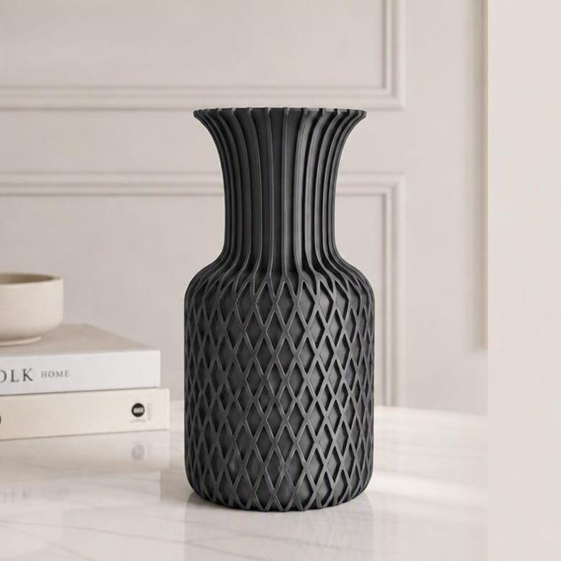 May include: A matte charcoal grey vase featuring a wide, flared rim and a textured, lattice-patterned body. The upper section of the vase displays vertical ridges that transition into a diamond-shaped grid pattern covering the lower portion.