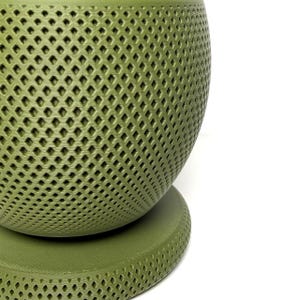 Puede incluir: Una maceta esf&eacute;rica de color verde oliva con un patr&oacute;n de celos&iacute;a en forma de diamante texturizado en toda su superficie. La maceta se asienta sobre una base circular a juego de color verde oliva, con un acabado mate y dise&ntilde;o geom&eacute;trico.
