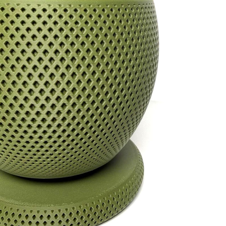 Puede incluir: Una maceta esf&eacute;rica de color verde oliva con un patr&oacute;n de celos&iacute;a en forma de diamante texturizado en toda su superficie. La maceta se asienta sobre una base circular a juego de color verde oliva, con un acabado mate y dise&ntilde;o geom&eacute;trico.