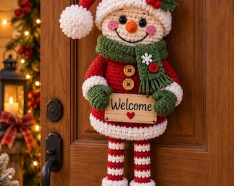 May include: A crocheted snowman wall hanging featuring a red hat with a white pom-pom, a green scarf with a snowflake, and a wooden sign that reads Welcome with a red heart. The snowman has striped legs and green curled shoes with gold bells.