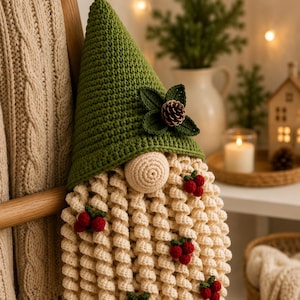 May include: A crocheted gnome wall hanging featuring a tall green pointed hat with a pinecone and leaf accent. The gnome has a round beige nose and a long, curly cream-colored beard decorated with several small clusters of red berries.