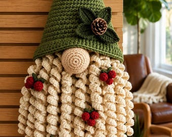 May include: A crochet gnome wall hanging featuring a tall green pointed hat adorned with a small pinecone and dark green leaves. The gnome has a round beige nose and a long, curly cream-colored beard decorated with several clusters of red berries.