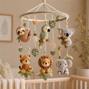 Peut inclure: Un mobile de chambre d'enfant suspendu composé de six figurines d'animaux au crochet, dont un paresseux, un perroquet, un koala, un tigre, un lion et un éléphant. Les éléments sont suspendus à un cercle recouvert de laine verte avec des feuilles.