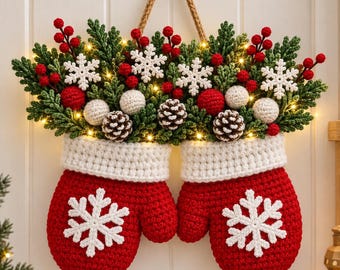 May include: A pair of red crocheted mittens with white snowflake appliqués, topped with green foliage, red berries, white pom-poms, and brown pinecones. The arrangement is illuminated by small warm lights and hangs from a braided jute rope.