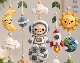 May include: A crochet baby mobile featuring a wooden ring decorated with white flowers and green leaves. Hanging elements include a yellow crescent moon, a blue planet with rings, a white cloud, an astronaut on a moon, a rocket, a sun, and stars.