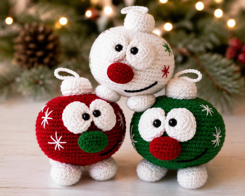 May include: Three round, crocheted ornaments featuring cartoon-like faces with large white eyes, black pupils, and round noses. One ornament is white with red and green accents, one is red with white snowflakes, and one is green with white snowflakes.