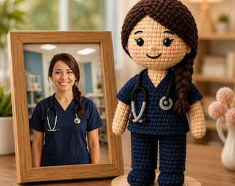 May include: A crochet doll featuring dark brown hair in a side braid, wearing a navy blue scrub top and matching pants. The doll has a small stethoscope accessory around its neck and stands on a round wooden base next to a framed photograph.