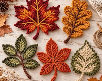 May include: A collection of five crocheted leaf appliques in various shapes and colors, including a large red and orange maple leaf, a golden yellow oak leaf, a green compound leaf, a bright orange leaf, and a green and cream-colored leaf.