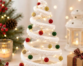 May include: A spiral-shaped Christmas tree made of white crocheted yarn, featuring a star topper and a brown crocheted base. The tree is decorated with small, hanging spherical ornaments in red, green, and gold, and illuminated by thin string lights.