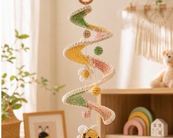 May include: A hanging crochet mobile featuring a spiral-shaped structure in pastel green, yellow, and pink. The mobile includes small crocheted spheres, a white flower, and a yellow and black striped bee dangling from thin strings below.