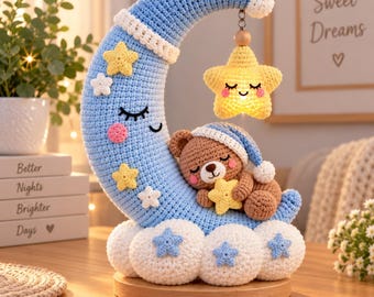May include: A crochet crescent moon in light blue with a sleeping face, adorned with small yellow and white stars. A brown teddy bear wearing a blue nightcap sleeps on the moon, holding a yellow star. A larger yellow star hangs from the moon.