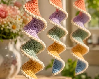 May include: Three hanging spiral ornaments crafted from crocheted yarn in a gradient of pastel colors including peach, lavender, mint green, yellow, and light blue. Each spiral features a cream-colored scalloped edge and hangs from a rope loop.