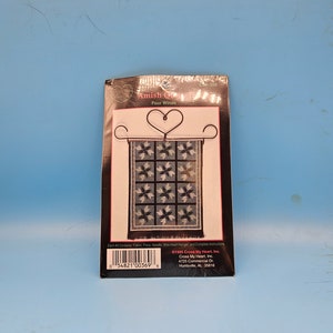 May include: A cross stitch kit featuring a blue and white quilt pattern with a heart-shaped wire hanger. The kit is titled "Amish Quilts Four Winds" and includes the text "©1995 Cross My Heart, Inc. Cross My Heart, Inc. 4725 Commercial Dr. Huntsville, AL 35816".