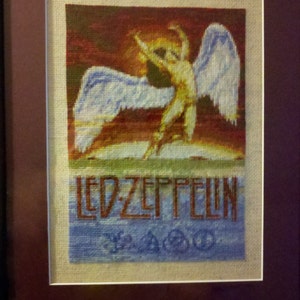 Puede incluir: Obra de punto de cruz enmarcada que representa una figura alada con el texto "LED ZEPPELIN" y un símbolo.