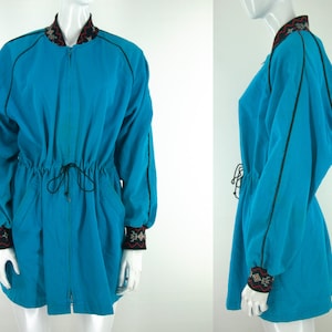 May include: A turquoise blue jacket with black trim and a drawstring waist. The jacket has a zipper closure and embroidered details on the collar and cuffs.