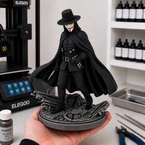 May include: A detailed black figurine of a character wearing a wide-brimmed hat, a long flowing cape, and a mask with a mustache and goatee. The figure stands on a circular, cracked stone-like base and holds small daggers in both hands.