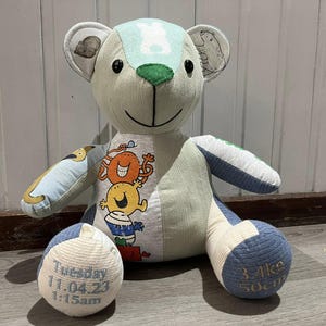 May include: A patchwork teddy bear constructed from various fabric panels in shades of light blue, green, and white. The chest features a graphic of stacked cartoon characters. The feet are embroidered with the text Tuesday 11.04.23 1:15am and 3.4kg 50cm.