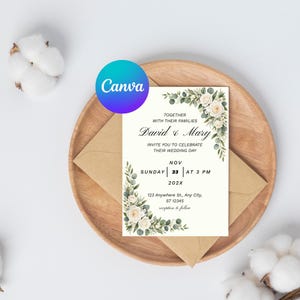 May include: A rectangular wedding invitation card featuring a floral border of white roses and green eucalyptus leaves. The text reads: Together with their families David & Mary invite you to celebrate their wedding day, Sunday Nov 23 at 3 PM 202X.