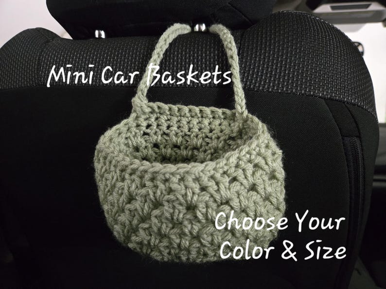Op de afbeelding: Een saliegroene gehaakte mand met &eacute;&eacute;n handvat, ontworpen om aan een hoofdsteun in de auto te hangen. De tekst "Mini Car Baskets" staat linksboven en de tekst "Choose Your Color & Size" staat rechtsonder in de afbeelding.