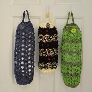 Puede incluir: Tres bolsas de crochet colgadas de ganchos en una puerta blanca. Las bolsas est&aacute;n hechas de hilo de diferentes colores, incluyendo azul, negro, blanco y verde. Cada bolsa tiene un bot&oacute;n en la parte delantera.
