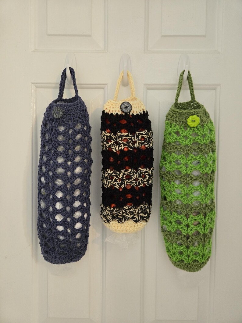 Puede incluir: Tres bolsas de crochet colgadas de ganchos en una puerta blanca. Las bolsas est&aacute;n hechas de hilo de diferentes colores, incluyendo azul, negro, blanco y verde. Cada bolsa tiene un bot&oacute;n en la parte delantera.