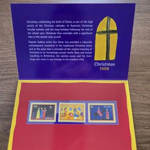 May include: A Christmas 1998 commemorative stamp sheet from Australia. The sheet features three stamps with religious imagery and text. The background is red, with a purple top and a yellow and purple design.