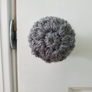 May include: A gray crocheted door knob with a circular design.