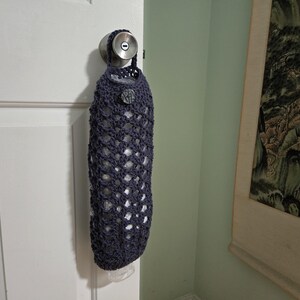 Puede incluir: Una bolsa de crochet azul oscuro con cierre de cord&oacute;n cuelga de un pomo de puerta. La bolsa est&aacute; hecha de un delicado patr&oacute;n de tejido abierto y est&aacute; dise&ntilde;ada para contener art&iacute;culos de comestibles.