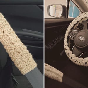 May include: Beige crochet seatbelt cover and steering wheel cover. The seatbelt cover is rectangular and fits over a gray seatbelt. The steering wheel cover is white and crocheted, with a decorative edge. The covers are designed for a car.