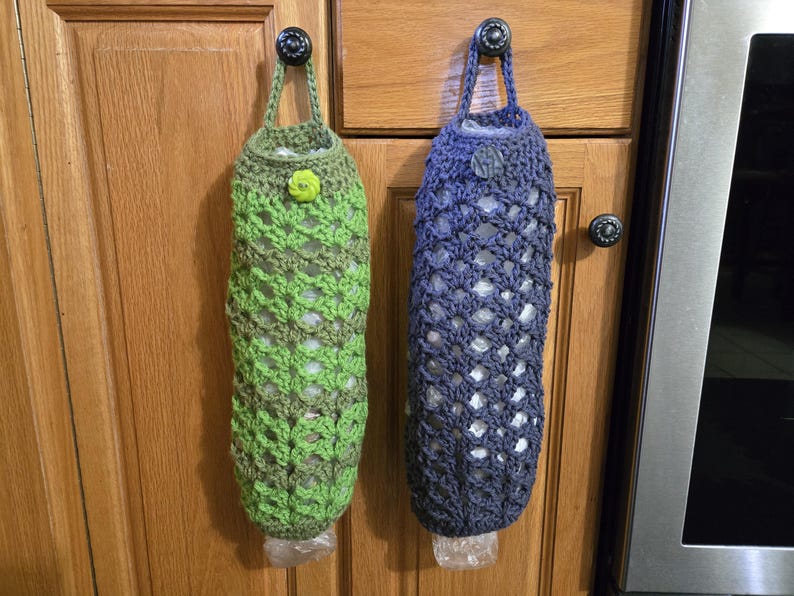 Puede incluir: Dos bolsas de crochet para guardar bolsas de pl&aacute;stico de la compra. Una bolsa es verde y la otra es azul. Ambas bolsas est&aacute;n colgadas de ganchos en una puerta de armario.