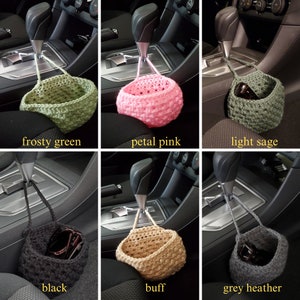 Op de afbeelding: Zes gehaakte auto-organizers in verschillende kleuren, waaronder frosty green, petal pink, light sage, zwart, buff en grijs heather. De organizers hangen aan de versnellingspook van een auto.