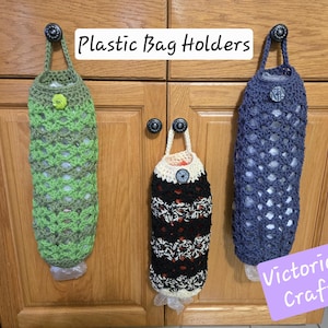 May include: Three crocheted plastic bag holders hanging on cabinet doors. The holders are green, black and white, and blue. The text "Plastic Bag Holders" is written above the holders. The text "Victoria's Crafts" is written below the holders.