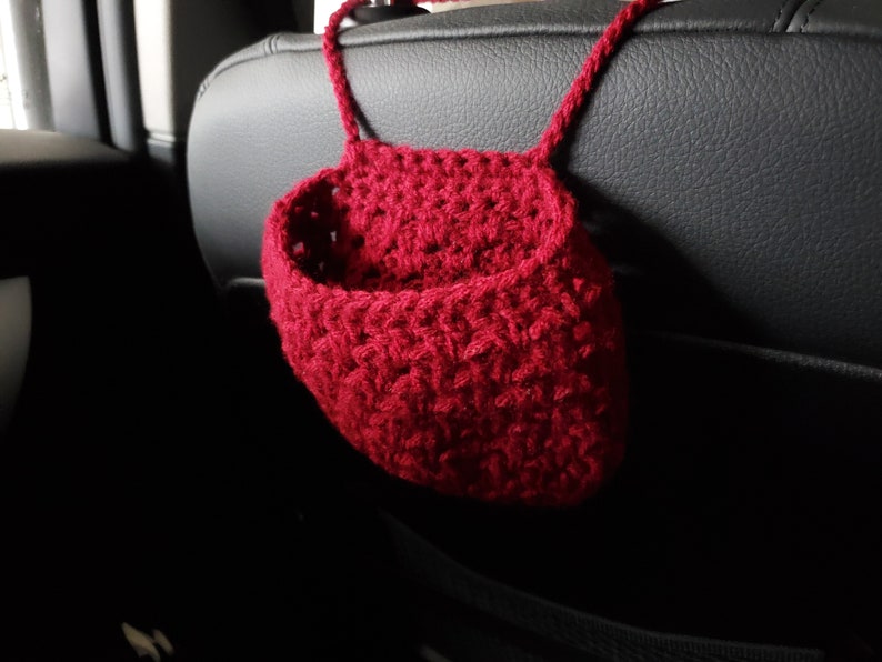 Op de afbeelding: Een rode gehaakte hangende organizer voor een auto. De organizer is gemaakt van dik garen en heeft een eenvoudig ontwerp.