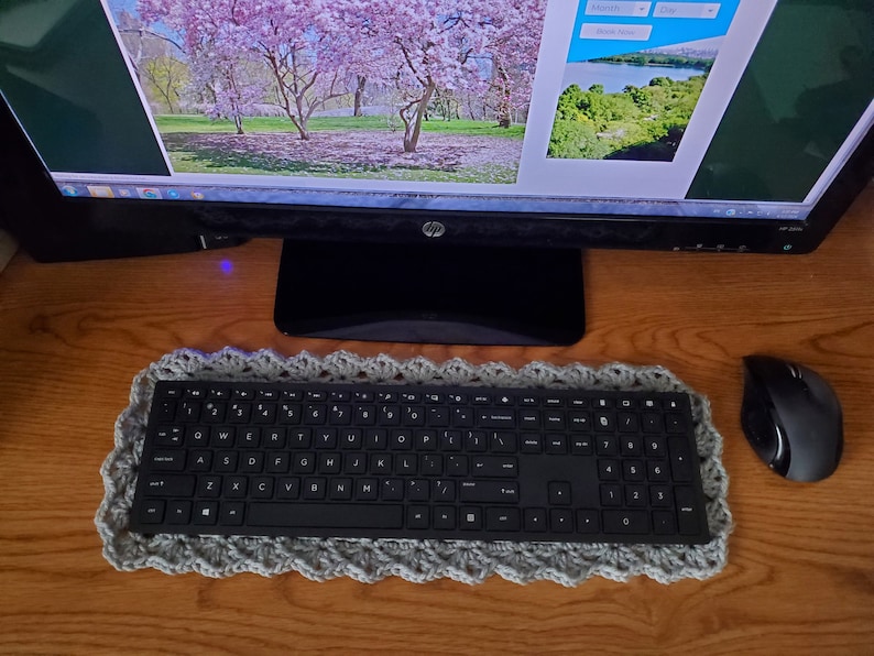 May include: A black computer keyboard with a gray crocheted keyboard rest. A black wireless mouse is on a wooden desk.