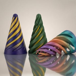 Peut inclure: Trois objets coniques avec des découpes en spirale. Le premier est violet avec des accents jaunes, le deuxième est vert foncé avec des accents jaunes, et le troisième présente un dégradé orange, violet et bleu sarcelle. Finition mate.