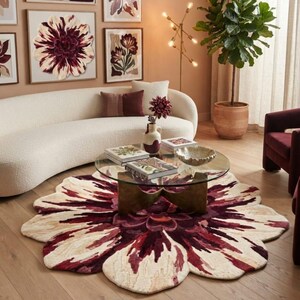 May include: A large, round, flower-shaped area rug featuring a deep burgundy, maroon, and cream-colored petal pattern. The rug is positioned beneath a circular glass coffee table with a gold-toned base, creating a focal point in the room.