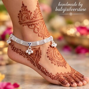 May include: A silver anklet featuring a fine mesh chain, small dangling bells, and blue stone accents. The anklet is worn on an ankle decorated with intricate brown henna patterns. The text handmade by balajisilverstore is visible.