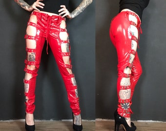 May include: Red leather trousers with multiple silver buckles and straps. The trousers have cutouts on the sides and a lace-up detail at the front.